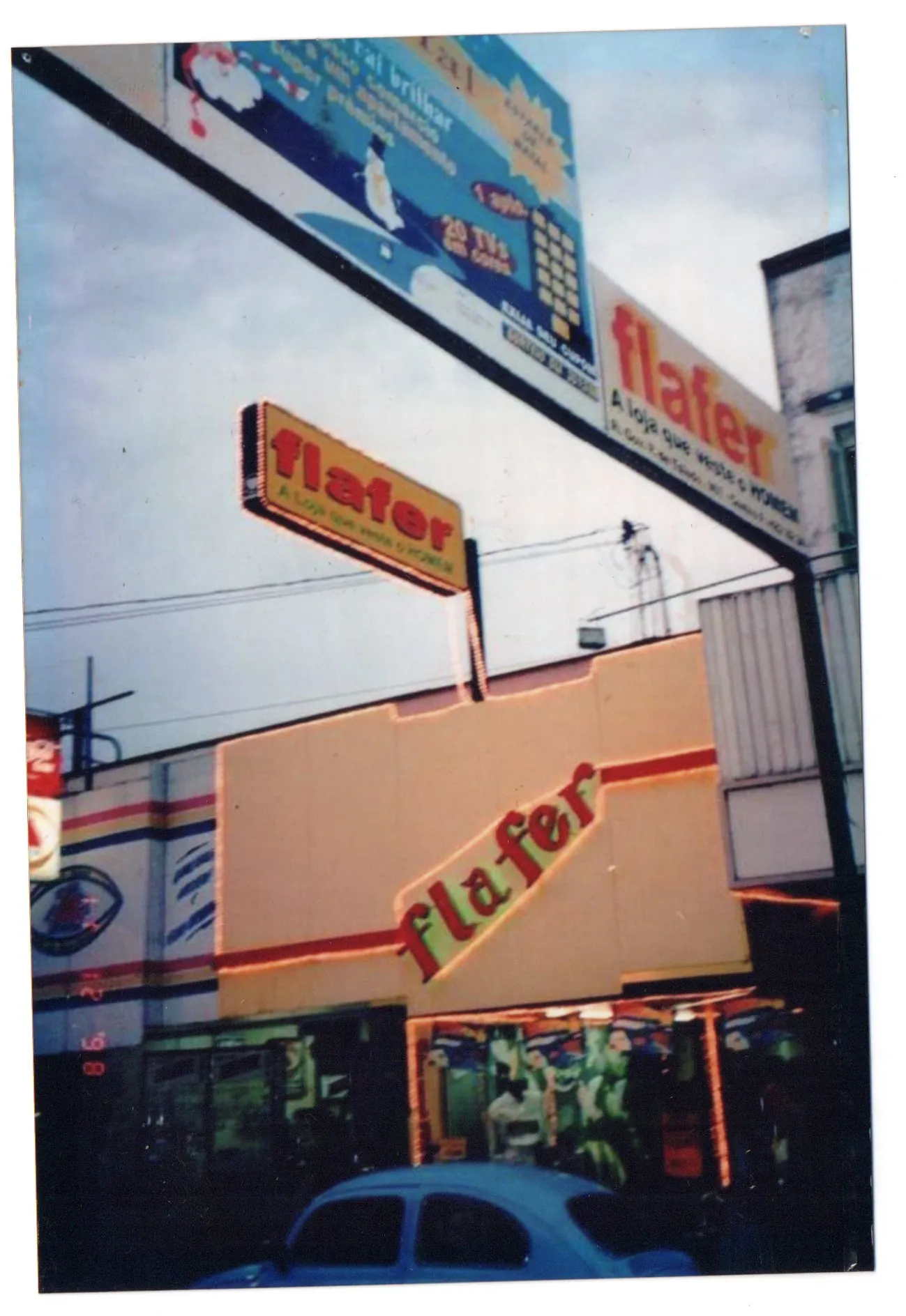 Fotografia colorida da fachada da Flafer com letreiros amarelos e vermelhos, incluindo uma placa suspensa com o nome flafer e a frase "a loja que veste você"